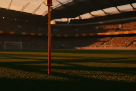 Empty floodlit stadium pitch at dusk with dramatic shadows and packed stands, golden-hour kick-off atmosphere.