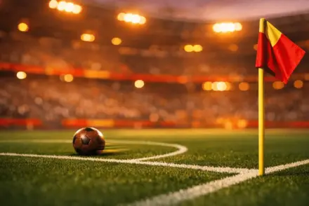 Floodlit stadium corner with red and gold accent lighting, football on centre pitch, low-angle evening shot.