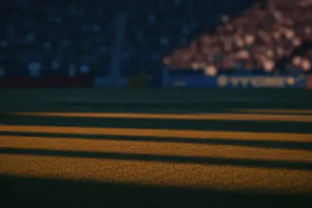 Empty floodlit football pitch at golden hour with packed stadium stands blurred behind, low-angle perspective with dramatic shadows.