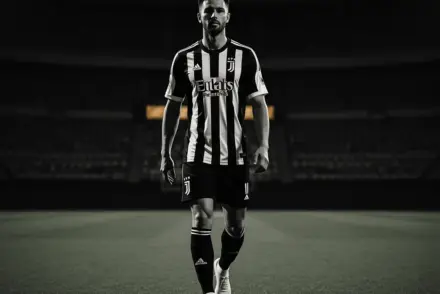 Footballer in black and white striped jersey walking confidently in stadium with dramatic lighting