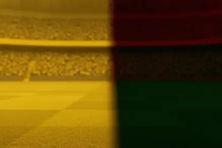 Empty floodlit stadium at golden-hour with dramatic shadows, yellow and red-green atmospheric lighting divide the pitch.