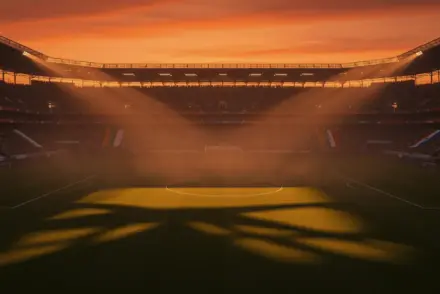 Floodlit stadium at golden-hour with packed stands, dramatic shadows, and empty pitch under cinematic lighting.