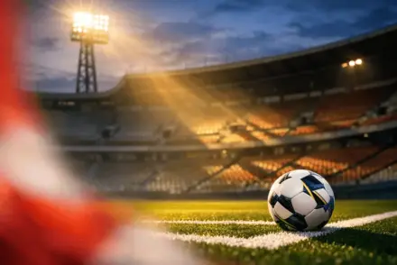 Empty stadium corner at night with red-white lighting accents, match ball on touchline, dramatic shadows on stands.