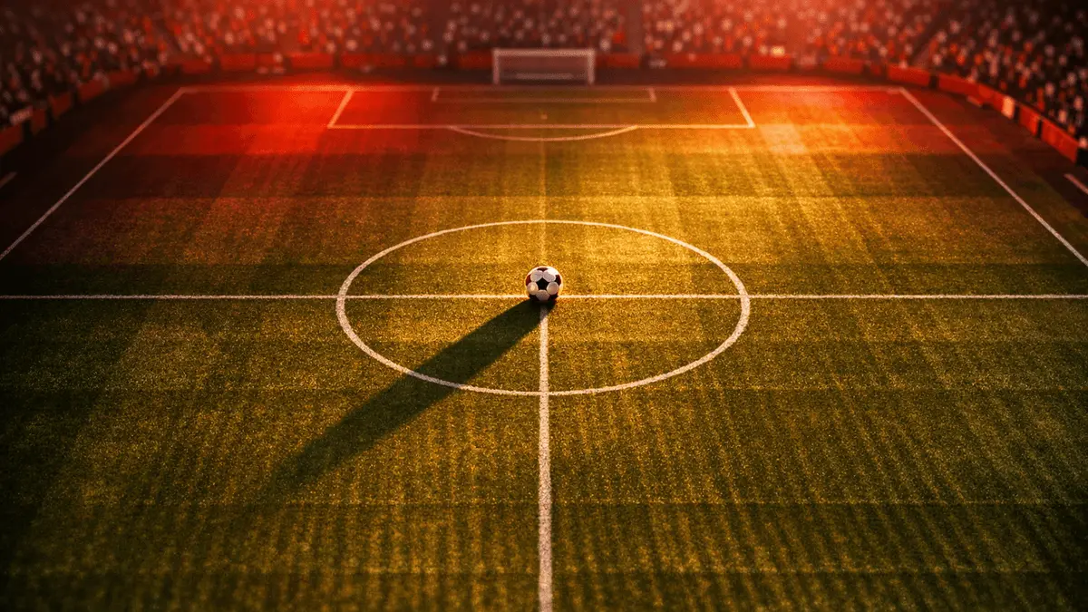 Overhead view of floodlit football pitch with ball on centre spot, illuminated in red and white lighting at dusk.