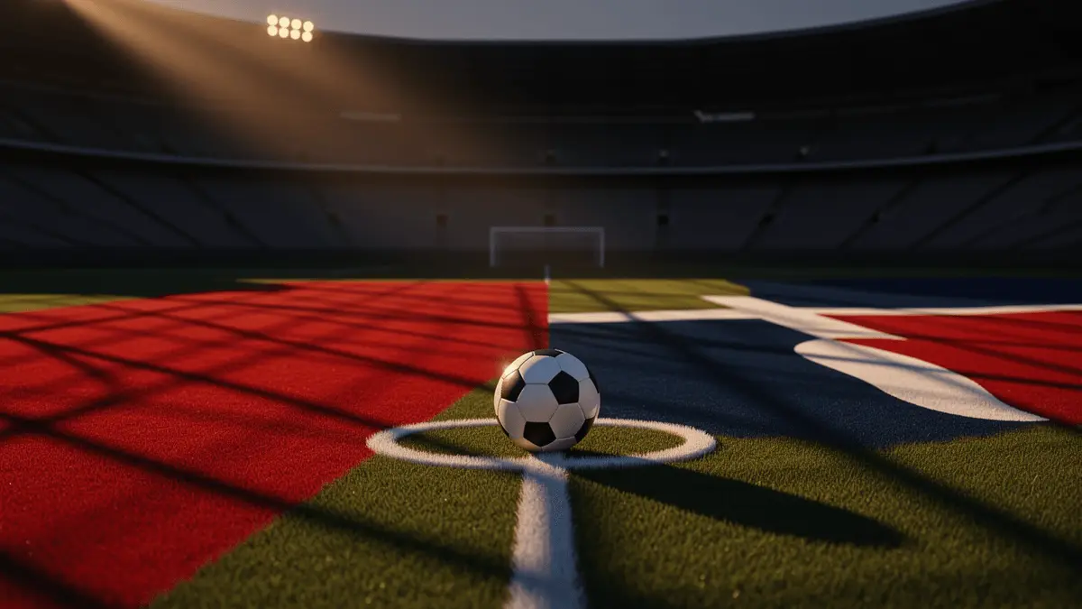 Evening stadium pitch with red-white and blue-red colour blocking, match ball in penalty arc, dramatic floodlight shadows.