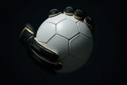 Goalkeeper hands gripping football in dramatic black and white lighting with gold accent detail