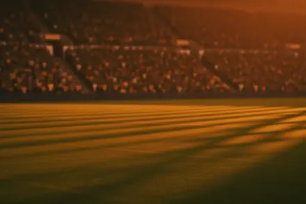 Floodlit stadium at dusk with packed stands, pristine pitch, dramatic shadows, and golden ambient lighting.