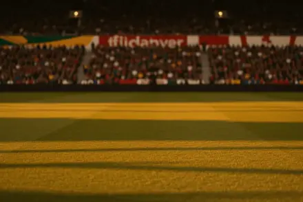 Floodlit football stadium at sunset with packed stands showing South African green and Canadian red colours, dramatic shadows on unmarked pitch, low sideline angle.