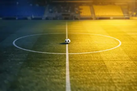 Aerial view of empty floodlit football pitch at dusk, blue and yellow light, centre circle marked, Sweden national colours.