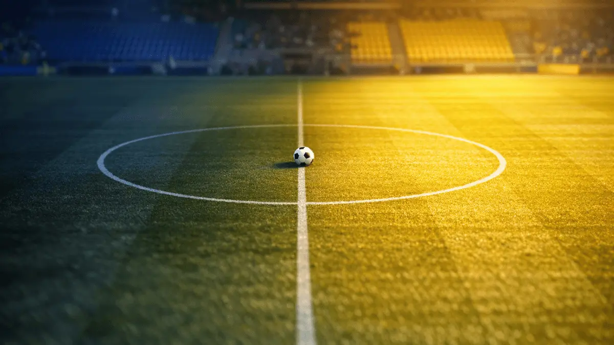 Aerial view of empty floodlit football pitch at dusk, blue and yellow light, centre circle marked, Sweden national colours.