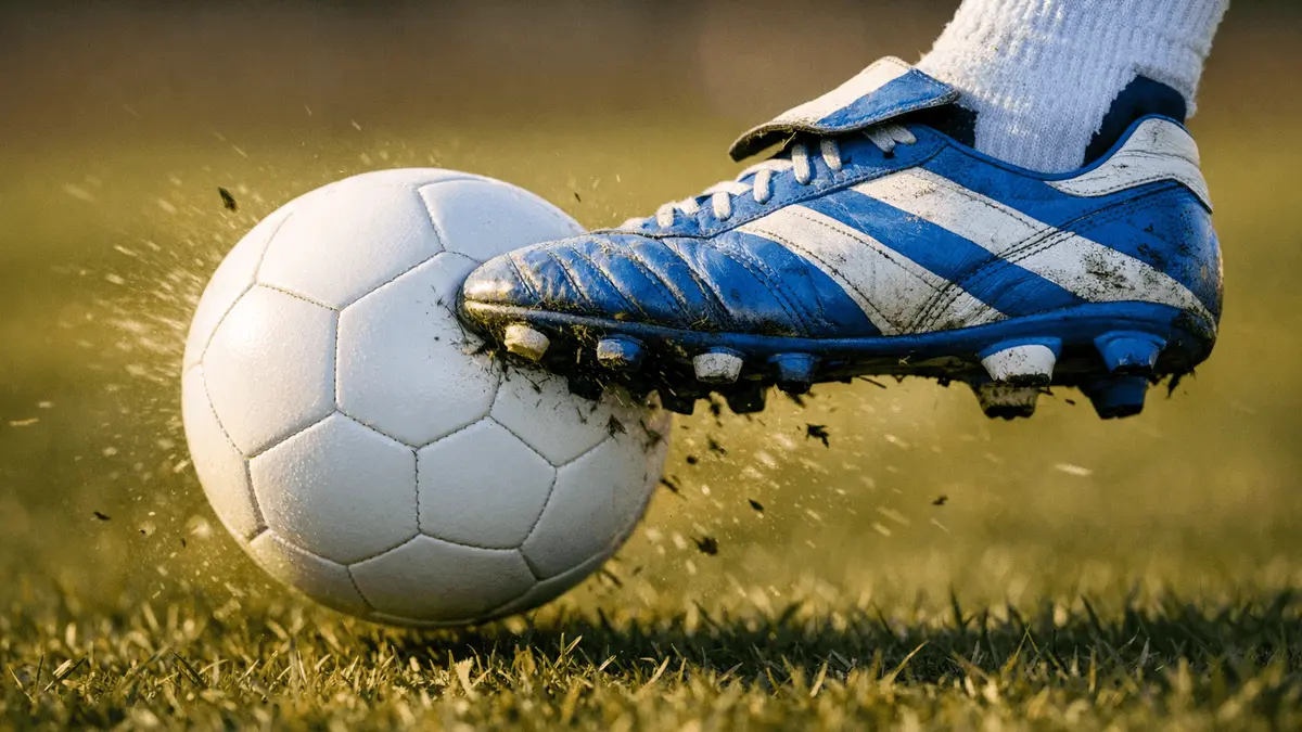 Football boot striking match ball in motion, blue and white colour palette, shallow depth of field, golden lighting.