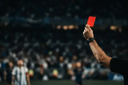 Referee holding red card in World Cup final with blurred Argentina players in background