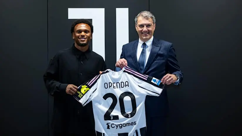 Loïs Openda and a Juventus official holding up a white Juventus jersey with the name Openda and number 20.