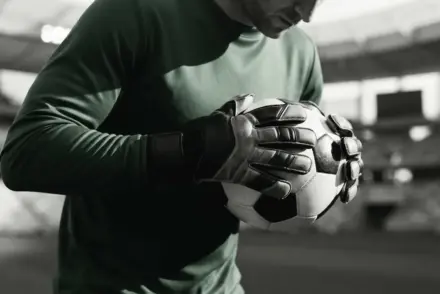 Goalkeeper hands gripping football in protective stance at Premier League stadium