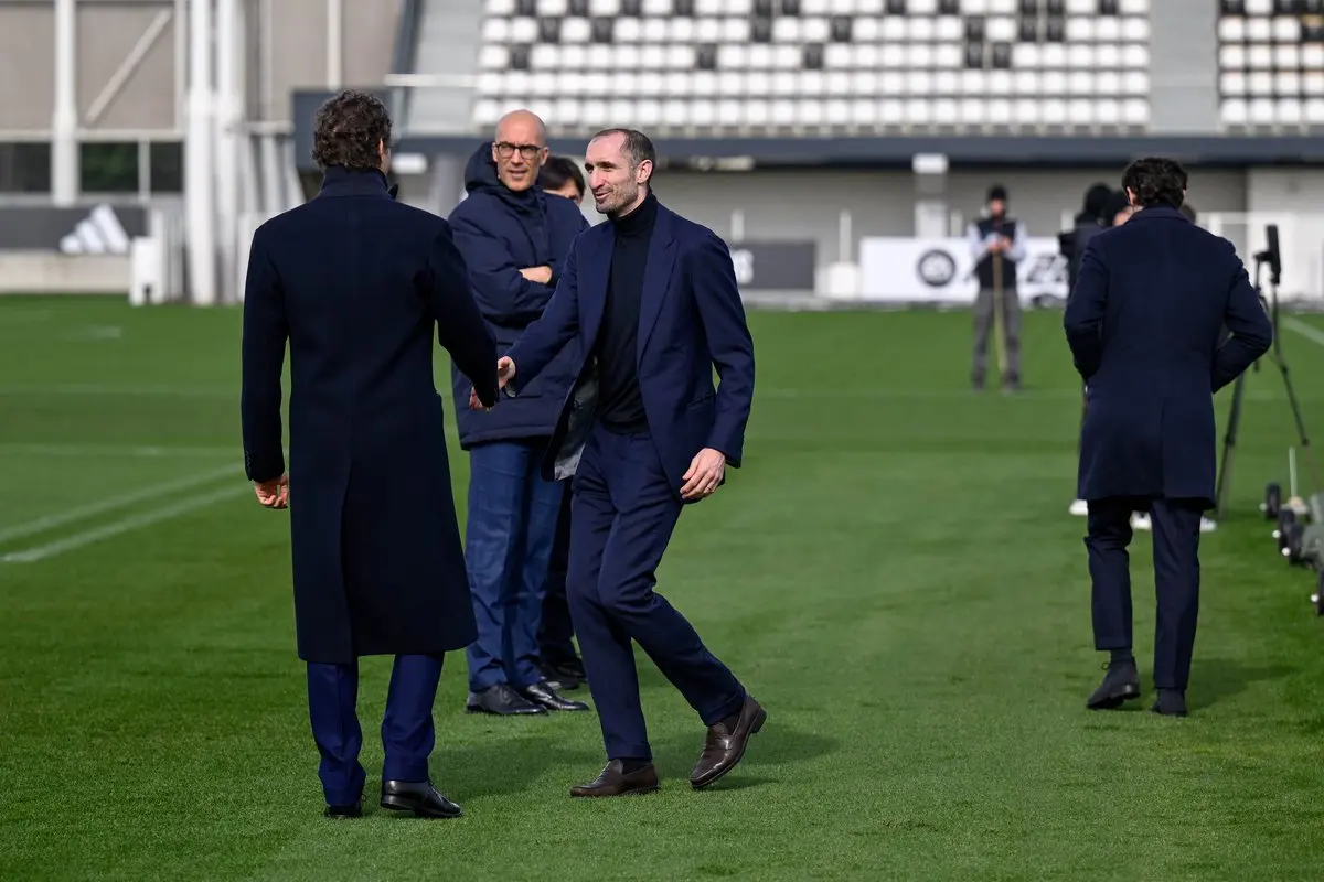 John Elkann shaking hands with Luciano Spalletti on a football pitch.