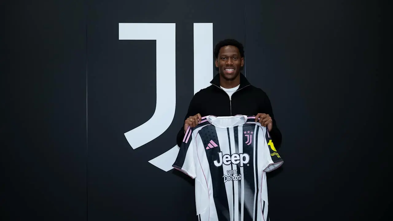 Moise Kean holding up a Juventus jersey in front of a large Juventus logo