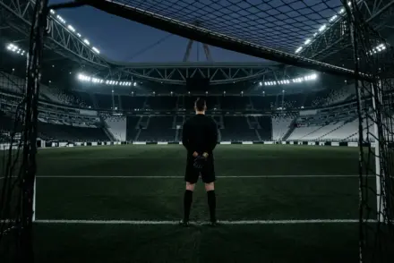 A Juventus-inspired goalkeeper stands behind the goal in a monochrome stadium scene with a subtle gold accent.
