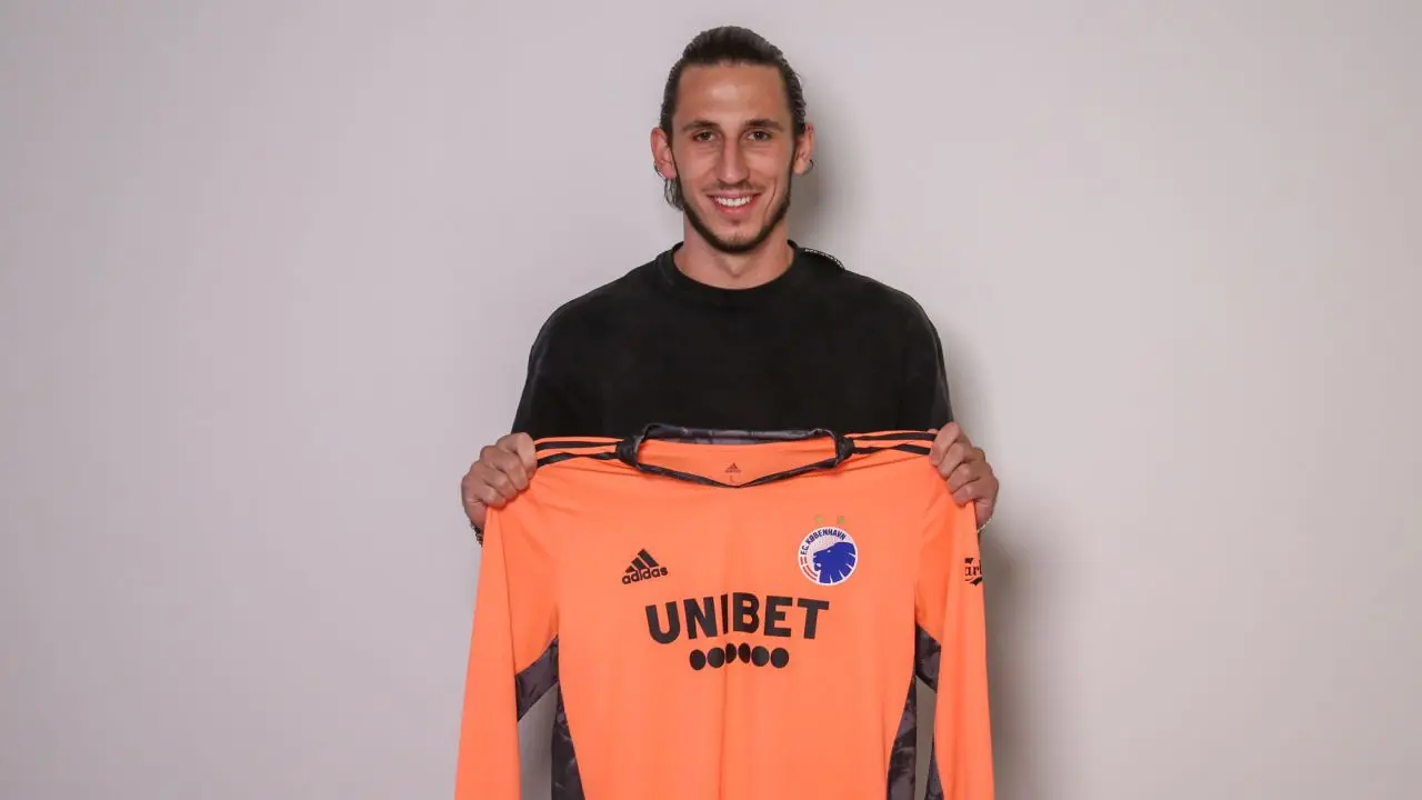 Kamil Grabara smiling and holding up an orange FC Copenhagen goalkeeper jersey