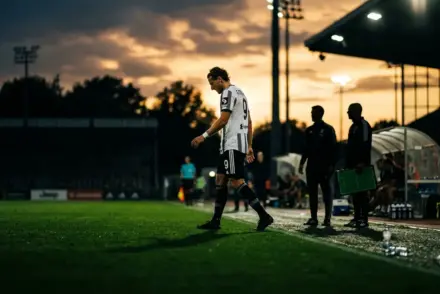 Football striker in black and white being substituted during pre-season match under stadium lights
