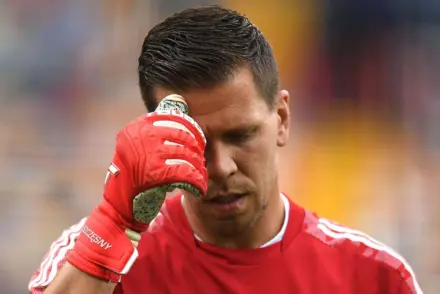 Juventus goalkeeper Wojciech Szczęsny in a red jersey and gloves, wiping his forehead.