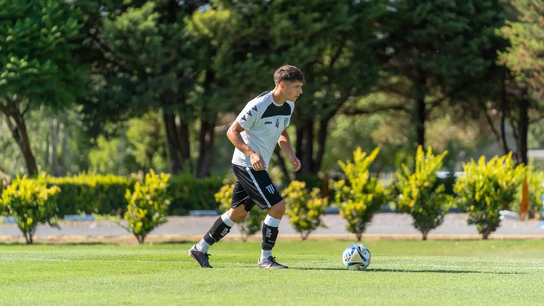 Kenan Yildiz in a white and black Juventus training kit dribbling a soccer ball on a green field.