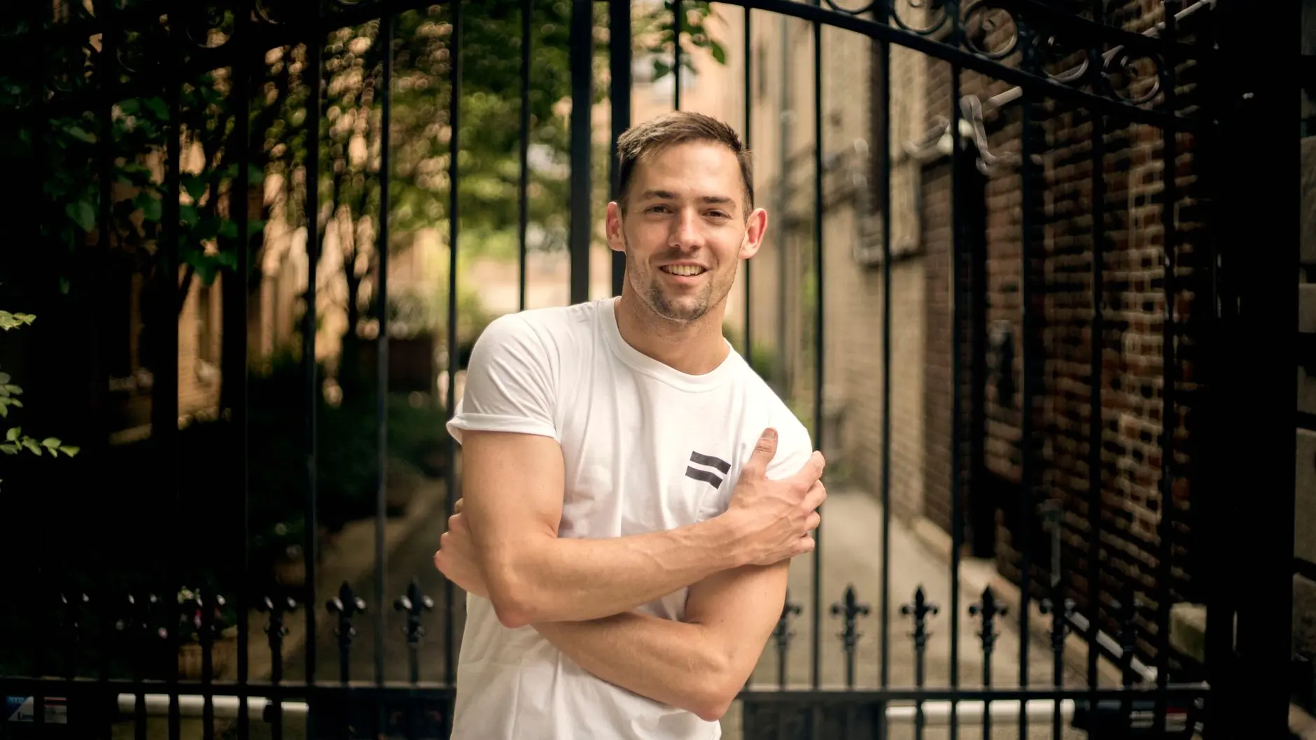 Portrait of Nick Woltemade wearing a white t-shirt and smiling in front of a black wrought iron gate.